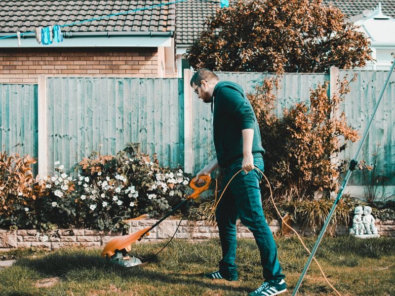 Worker running a string trimmer along a backyard fence line